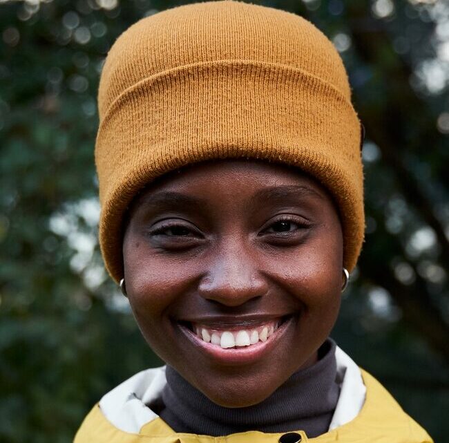 Cheerful portrait of a young African woman looking at camera with a toothy smile standing outdoors.