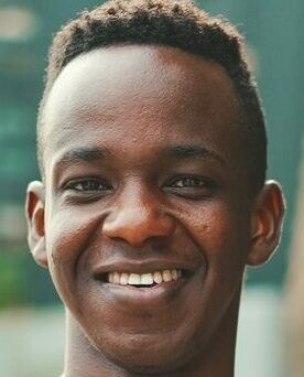 Young african student stands outside of university, looks at the camera, smiles